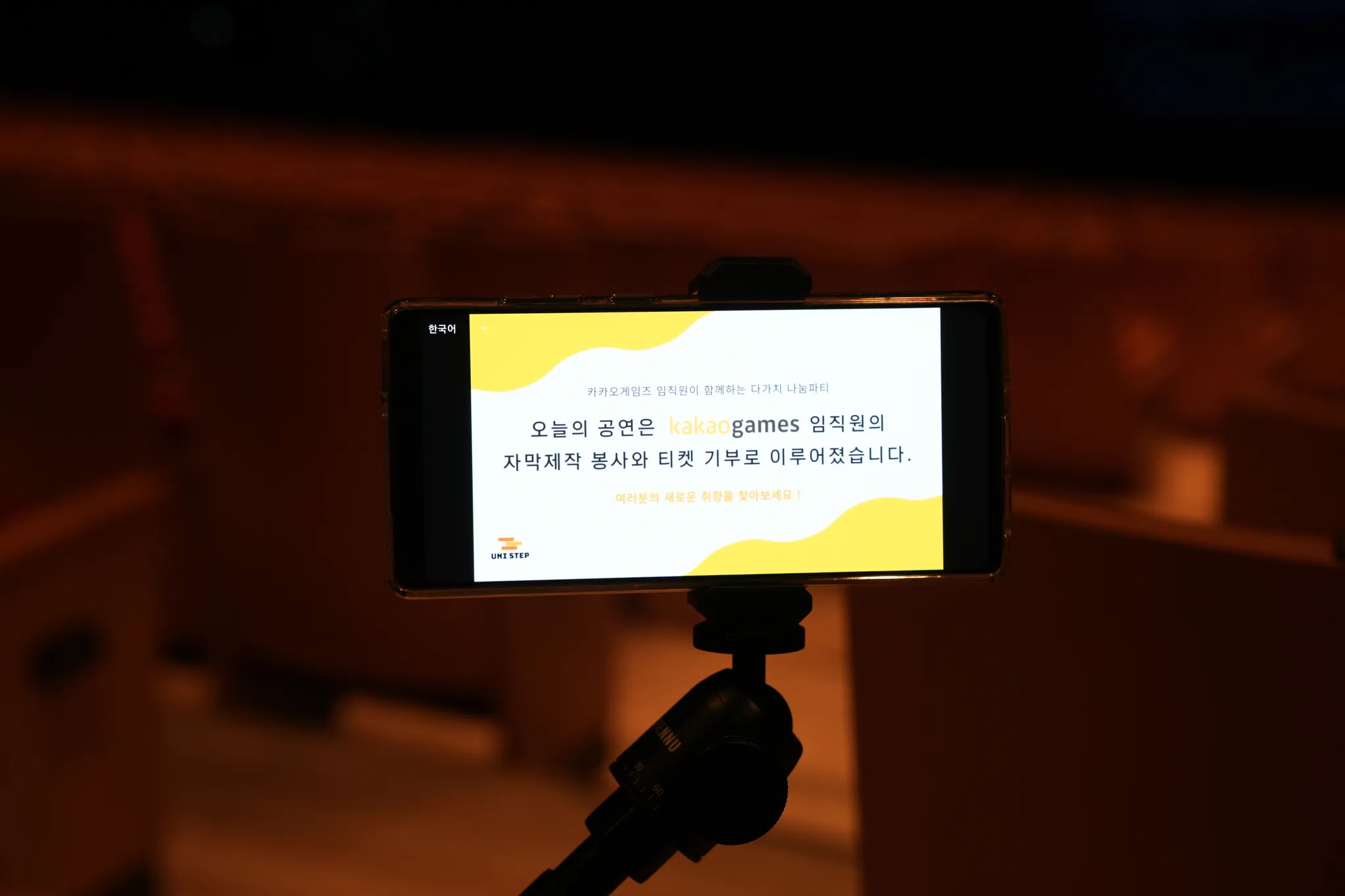 좌석 거치대 자막 단말기 화면(한국어) — "카카오게임즈 임직원이 함께하는 다가치 나눔파티 / 오늘의 공연은 kakaogames 임직원의 자막제작 봉사와 티켓 기부로 이루어졌습니다. / 여러분의 새로운 취향을 찾아보세요!" UNI STEP 로고