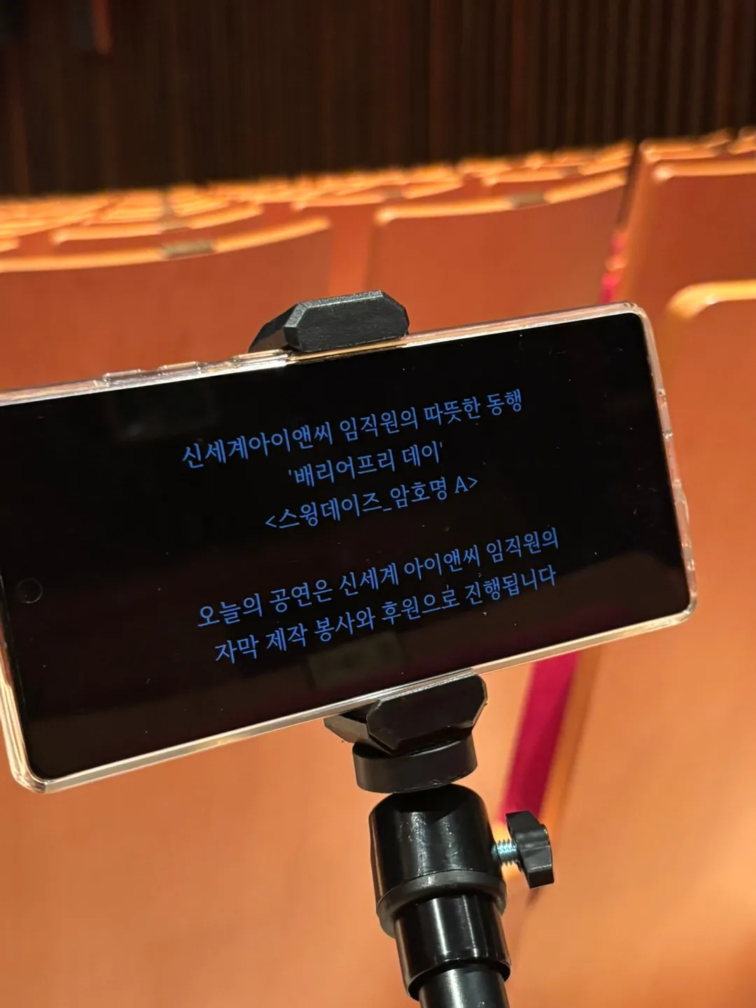 좌석 거치대 자막 단말기 화면 — "신세계아이앤씨 임직원의 따뜻한 동행 / '배리어프리 데이' / <스윙데이즈_암호명 A> / 오늘의 공연은 신세계 아이앤씨 임직원의 자막 제작 봉사와 후원으로 진행됩니다"